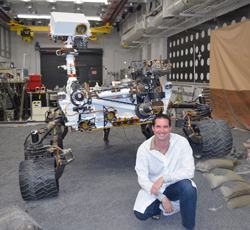 Brain Schratz poses in front of the engineering model of the mars science laboratory